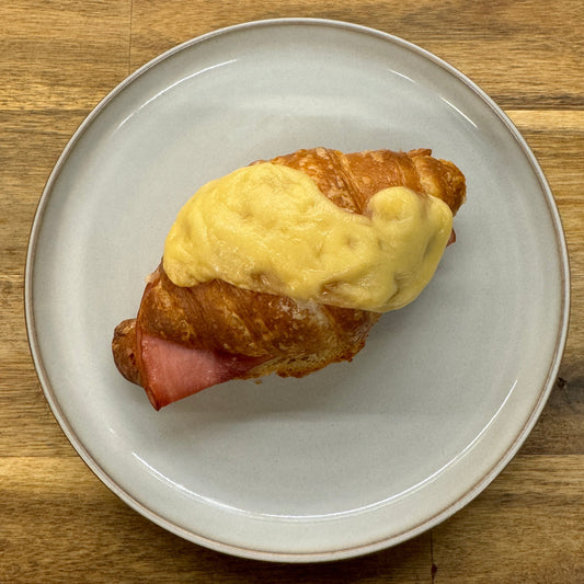 A tempting photo of a ham and cheese croissant showcasing its golden, flaky layers - Generously filled with savory ham and melted cheese, creating a mouthwatering combination of textures and flavors.