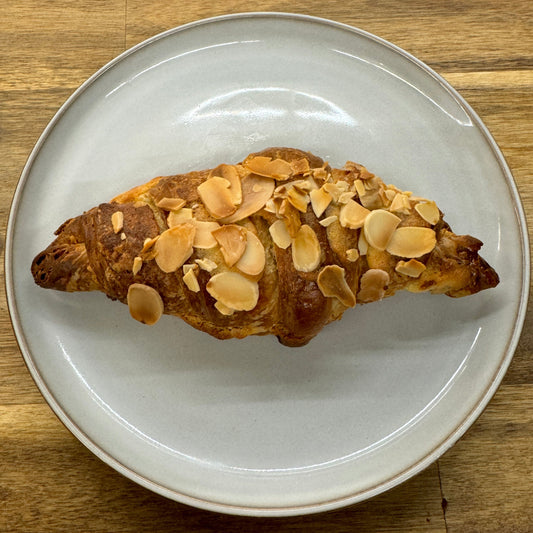 A tempting almond croissant with golden, flaky layers, generously adorned with toasted almond slices on top. 